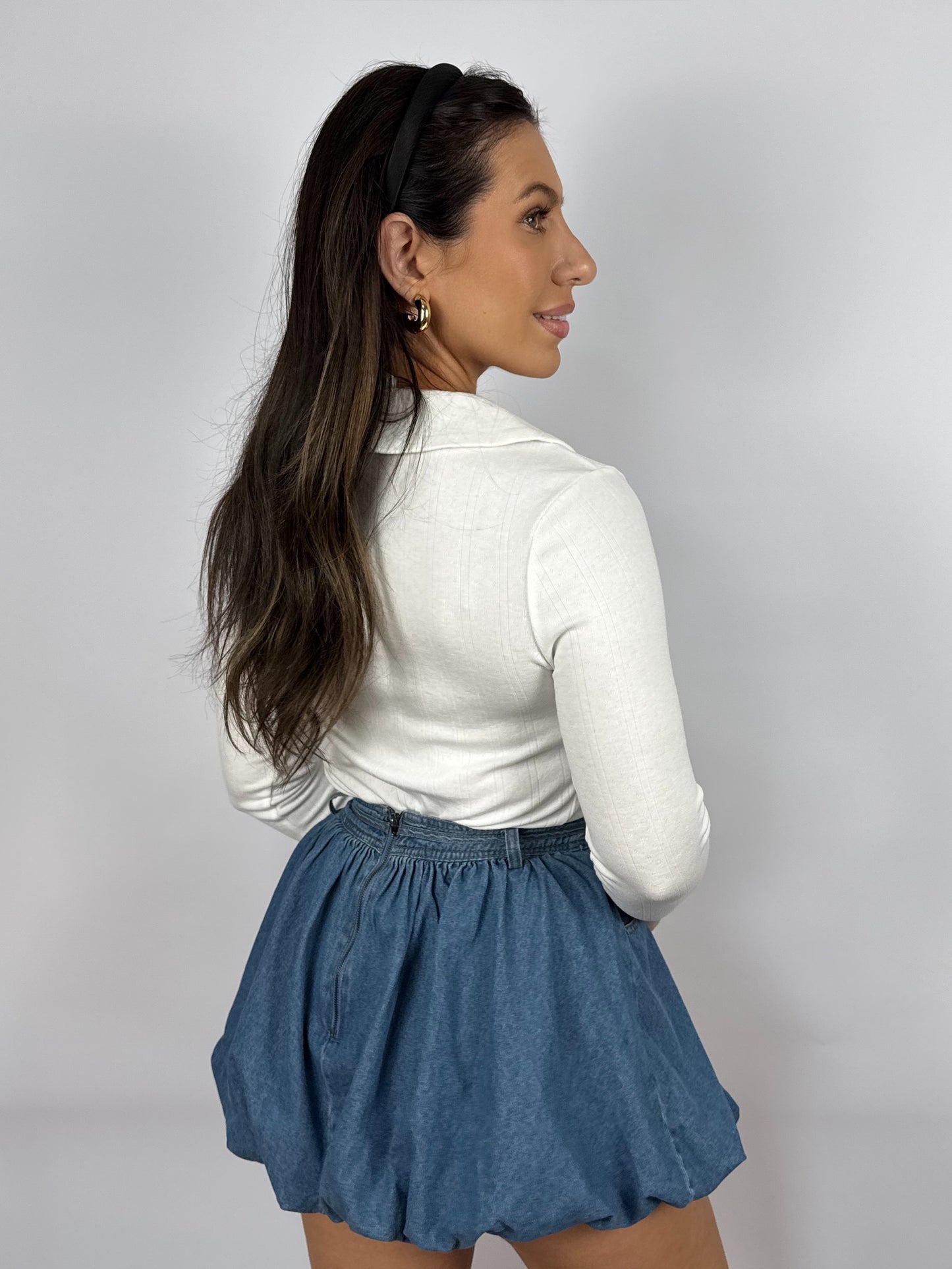 Back of Woman wearing a white pointelle long sleeve top with a Peter Pan collar and blue denim shorts on a plain background