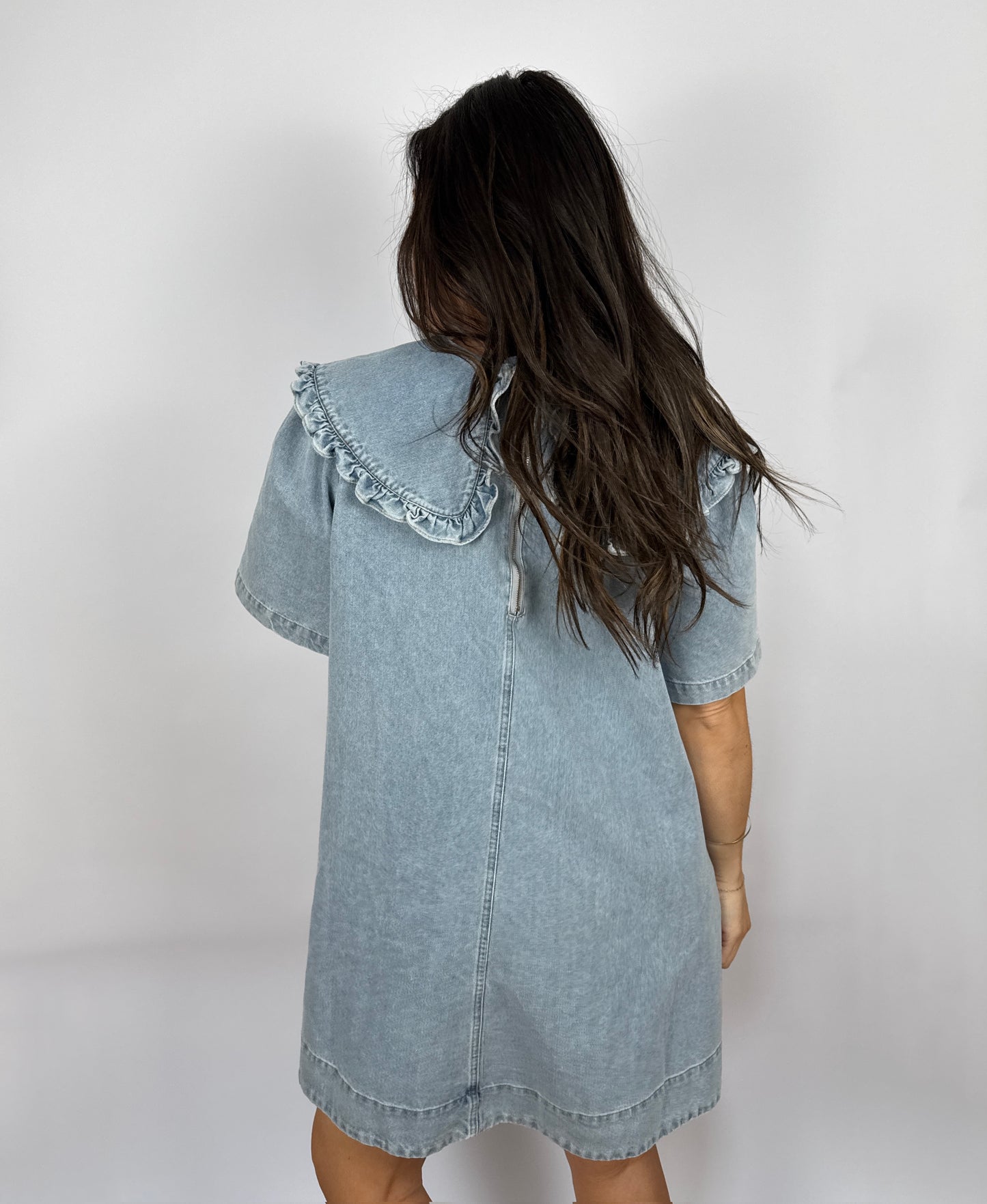 Woman wearing a denim dress with ruffled Peter Pan collar against a plain background