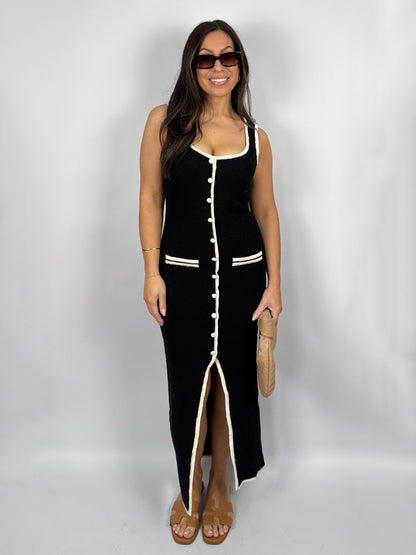 Woman wearing a black knit dress with white buttons and trim on a plain background