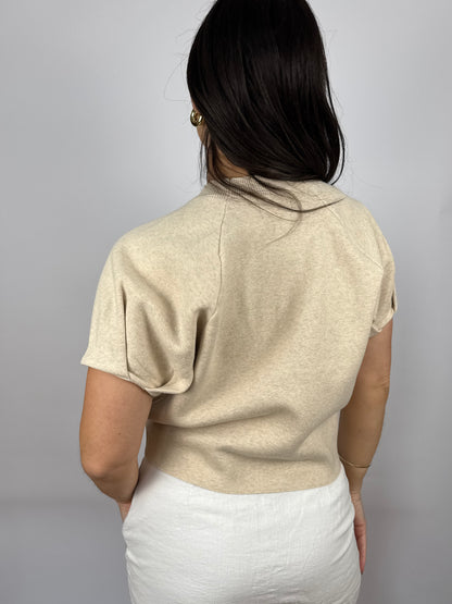 Person wearing a beige short-sleeve top against a gray background