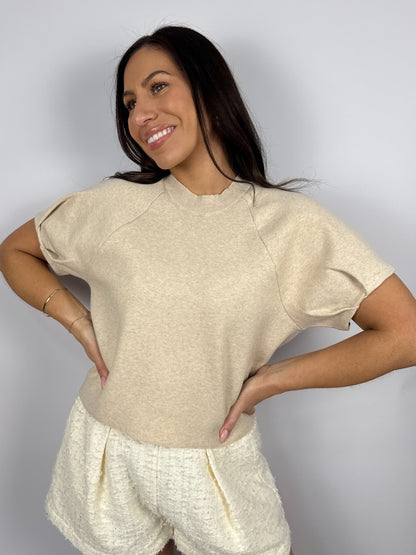 Woman wearing a beige sweater top and white shorts against a plain background