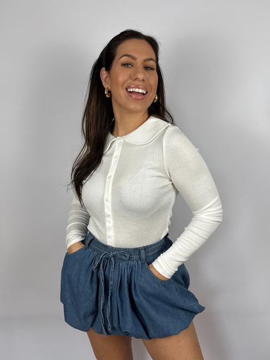 Woman wearing a white long-sleeve top and blue denim bubble hem skirt against a plain background