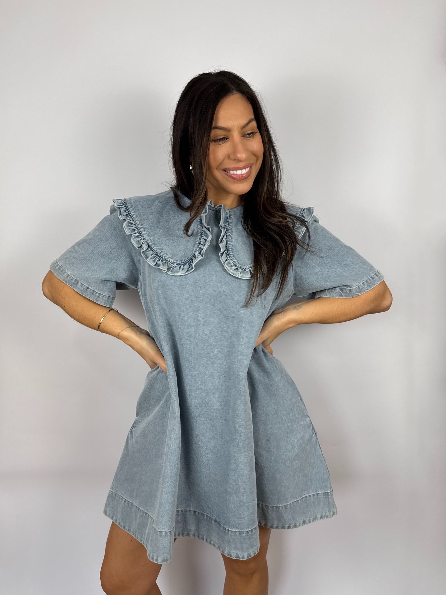 Woman wearing a denim dress with ruffled  Peter Pan collar against a plain background