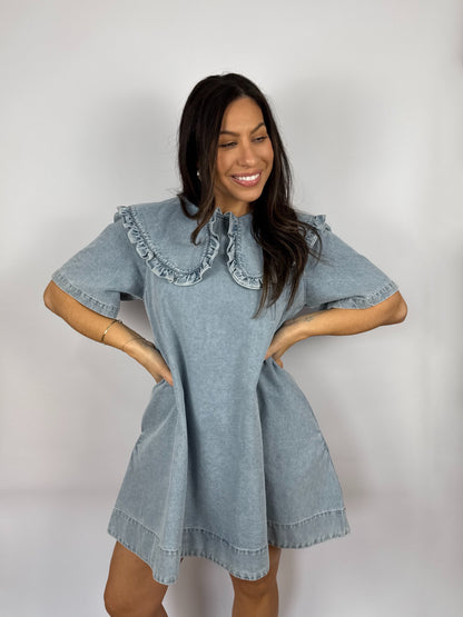 Woman wearing a denim dress with ruffled  Peter Pan collar against a plain background