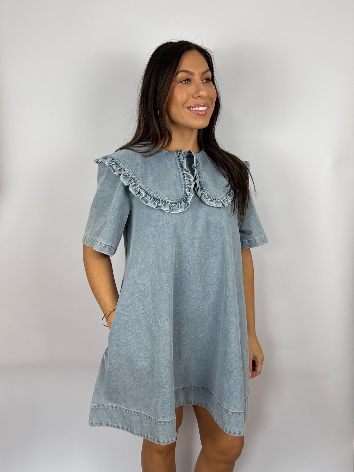 Woman wearing a denim dress with ruffled  Peter Pan collar against a plain background