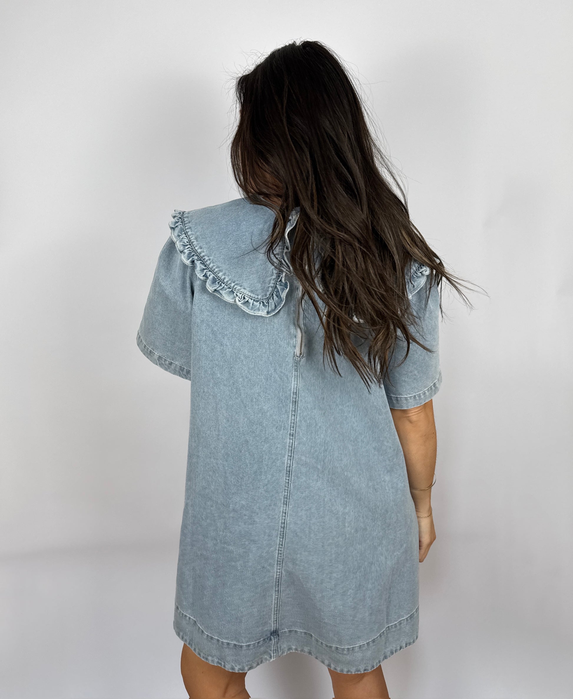 Woman wearing a denim dress with ruffled  Peter Pan collar against a plain background