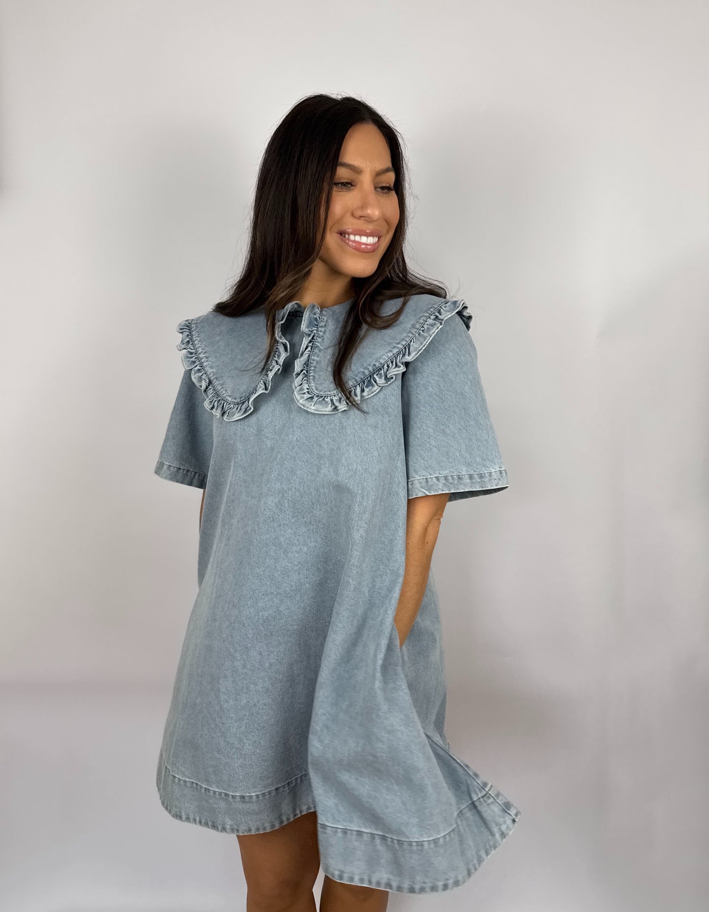 Woman wearing a denim dress with ruffled  Peter Pan collar against a plain background